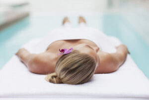 Eine Frau liegt entspannt auf einer Massageliege eines Pools in einem Wellnesshotel